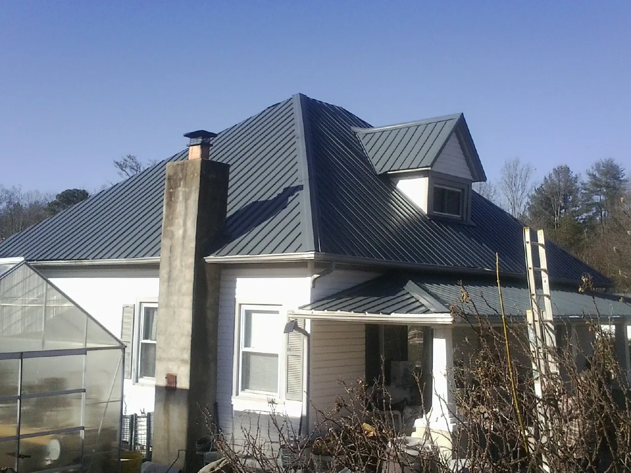 Dark blue standing seam metal roof on a white farmhouse with dormer — Slate & Tile Roof Repair by Roofing Brothers in Woodside
