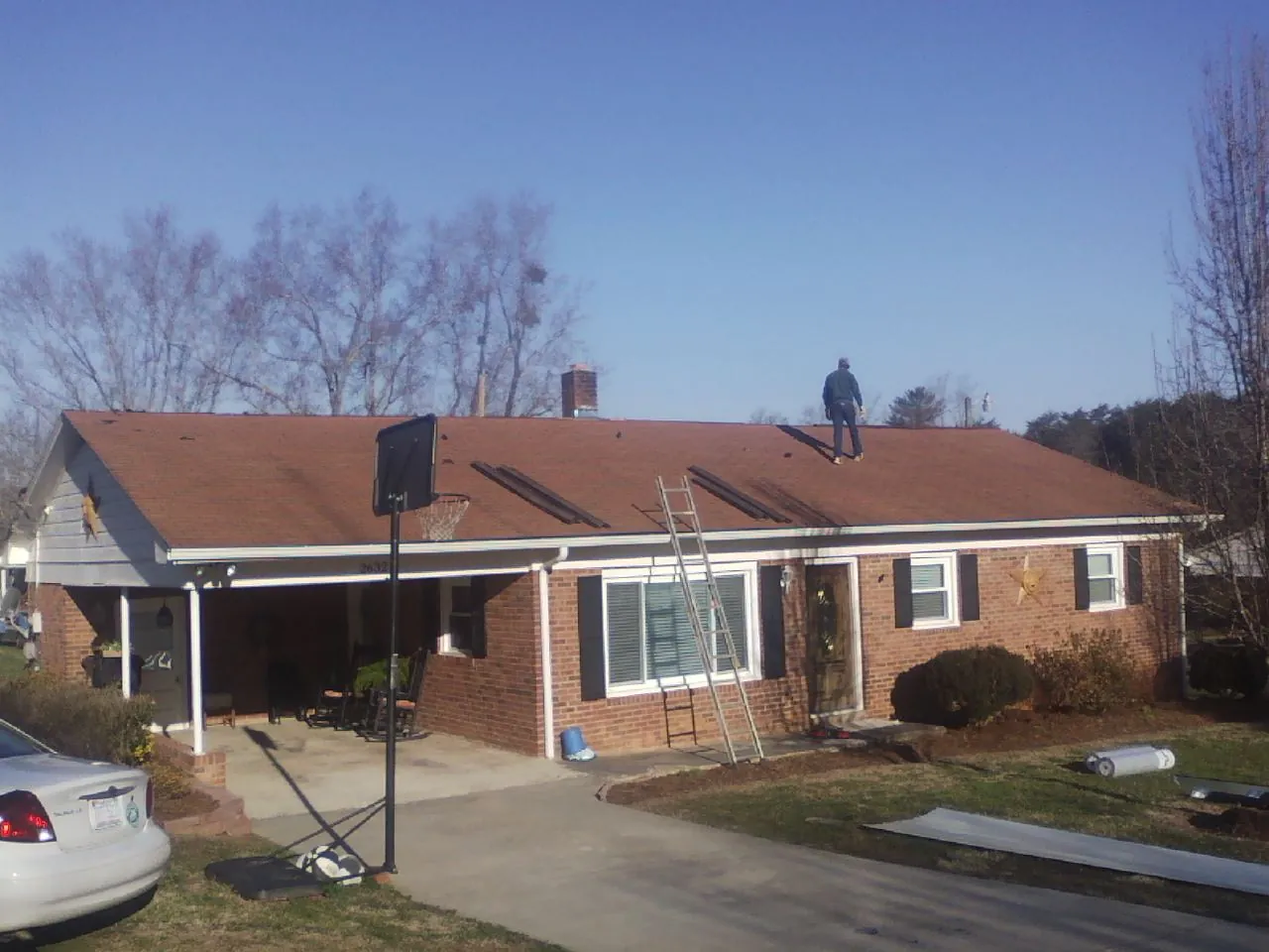 Roofer stripping a shingle roof on a brick ranch before metal panels in Woodside