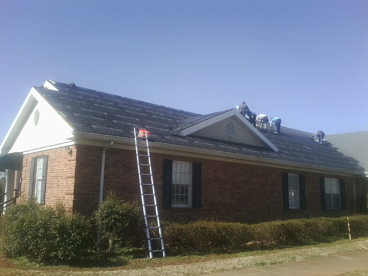 Crew tearing shingles off a brick ranch roof with a ladder set — Emergency Roof Repair work by our crew in Woodside