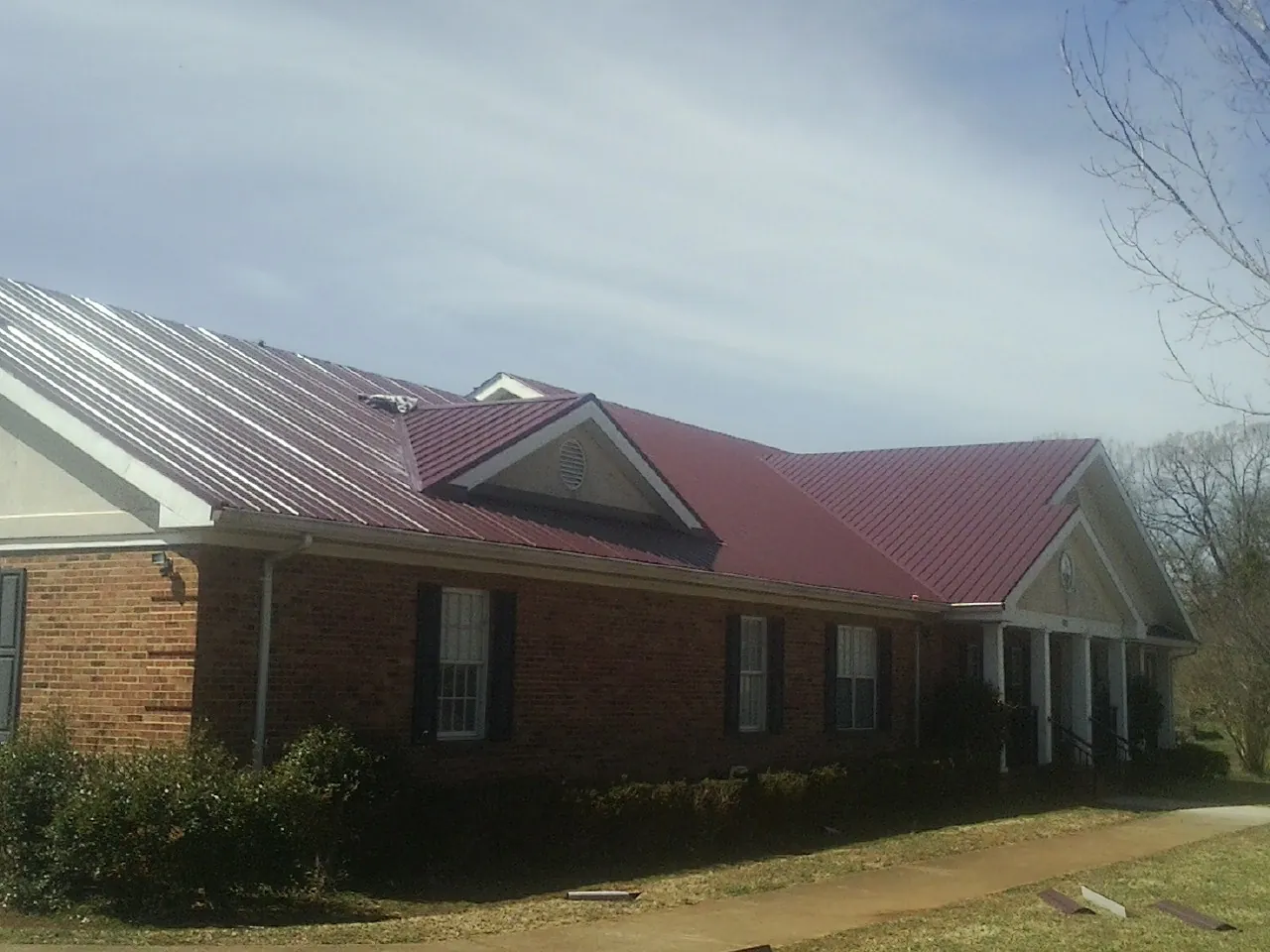 Red metal roof with gabled entries on a long brick building, from a Hail Damage Roof Repair job in Woodside