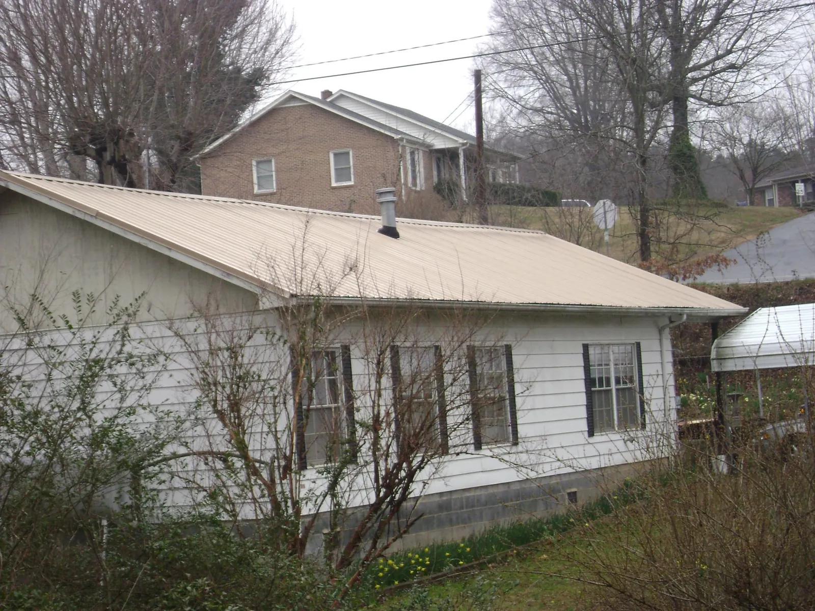 Tan metal roof on a white sided house set into a hillside — Commercial Roofing by Roofing Brothers in Woodside